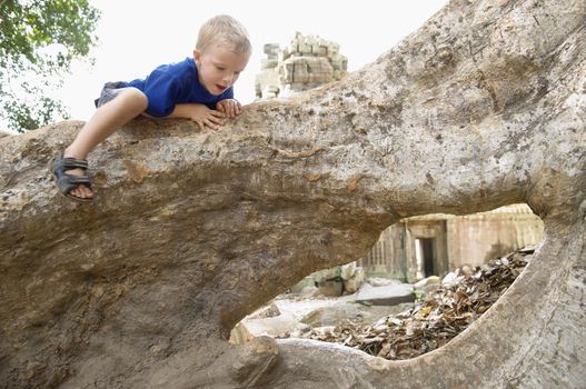 Little Boy Climbing on Tree Roots in Ruins