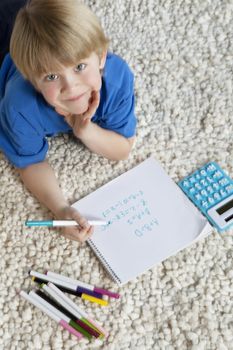 Portrait of blond hair boy lying on rug doing homework