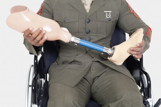 Midsection of a US military officer holding prosthesis leg as he sits in wheelchair
