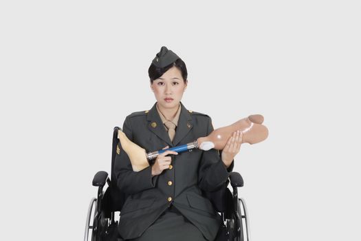 Female US military officer in wheelchair holding artificial limb over gray backgrounds