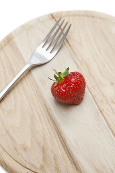 Cropped shot of wooden plate with strawberry and fork on it