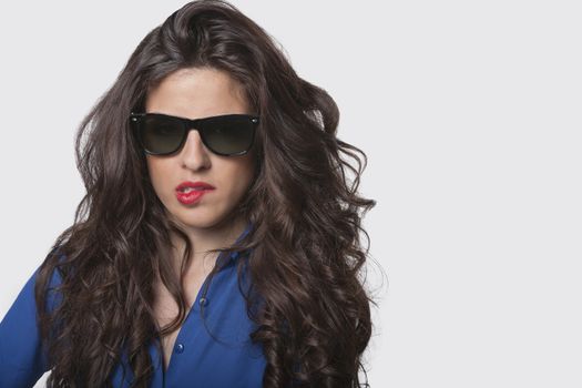 Portrait of sensuous young woman wearing sunglasses while biting lip over gray background