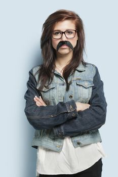 Portrait of young woman wearing eyeglasses and fake mustache against light blue background