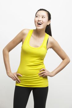 Happy young woman in yellow tank top with hands on hips looking away against white background