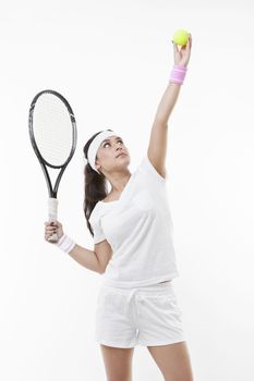 Young female tennis player preparing to serve ball against white background