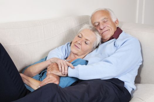 Romantic senior couple with arms around relaxing on sofa at home