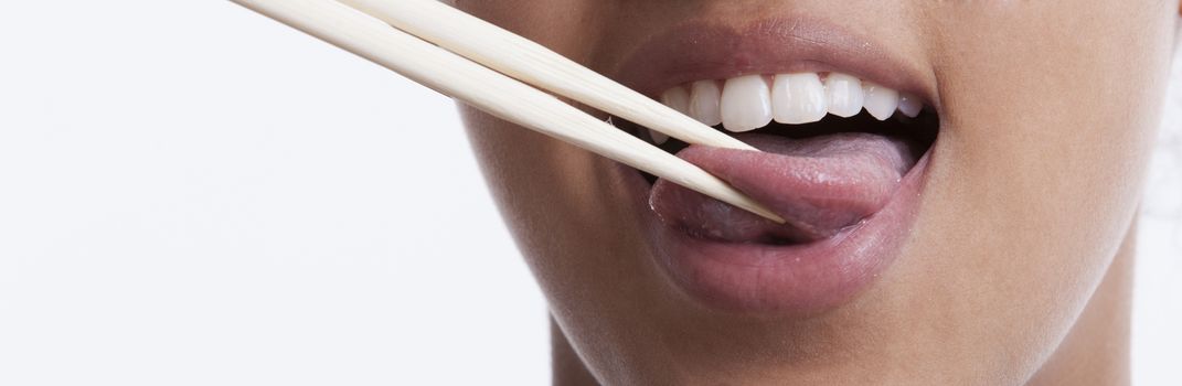 Playful young woman with chopsticks sticking out tongue against white background