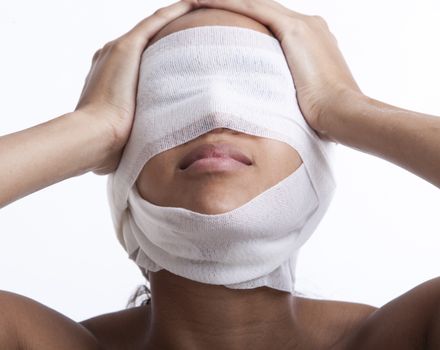 Young woman with head wrapped in bandage against white background