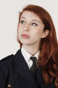 Thoughtful young woman in police officer's costume against gray background