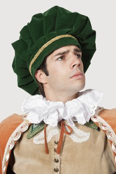 Thoughtful young man in old-fashioned costume looking away against gray background