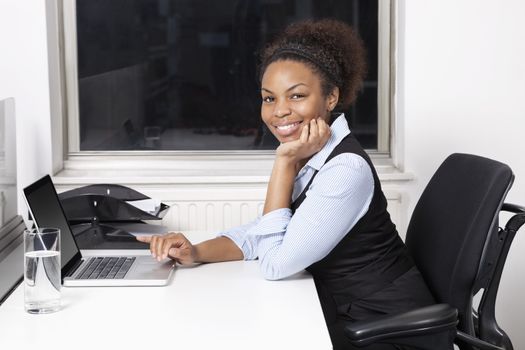Portrait of smiling young businesswoman using laptop at desk in office