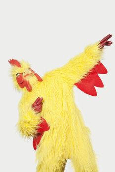 Playful young man in chicken suit against gray background