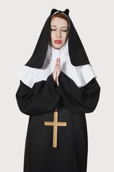 Young nun praying against gray background
