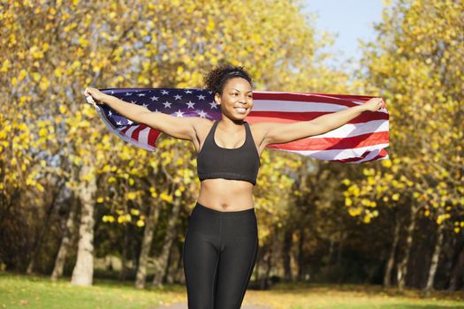 Happy young female holding up American flag in park