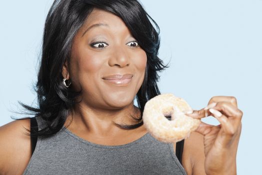 Overweight mixed race woman eating donut over blue background