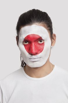 Portrait of serious young mixed race man with Japanese flag painted on face against white background