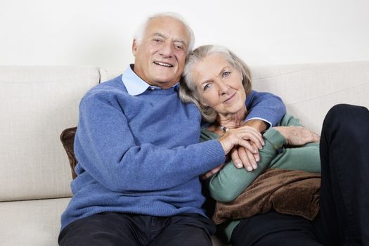 Portrait of happy elderly man with arm around spouse sitting on sofa at home