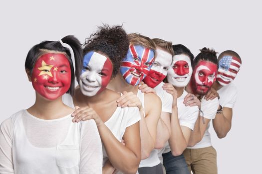 Portrait of happy Multi-ethnic group of friends with various national flags painted on their faces standing against white background