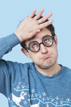 Geek young man wearing novelty glasses with hand on head over blue background