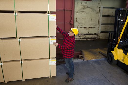 Worker inspecting wood pallet standing by fork lift truck