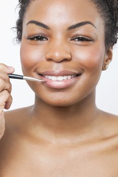 Close-up portrait of young woman applying lip gloss with brush