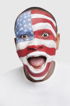 Portrait of surprised young man with North American flag painted on face shouting against white background
