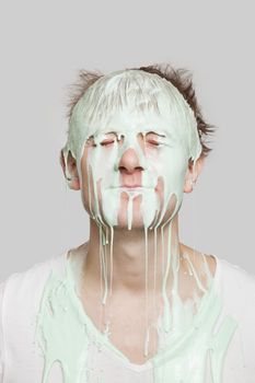 Paint dripping down a young Caucasian man's face against gray background