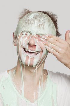 Young Caucasian man covered with paint wiping his eyes against gray background