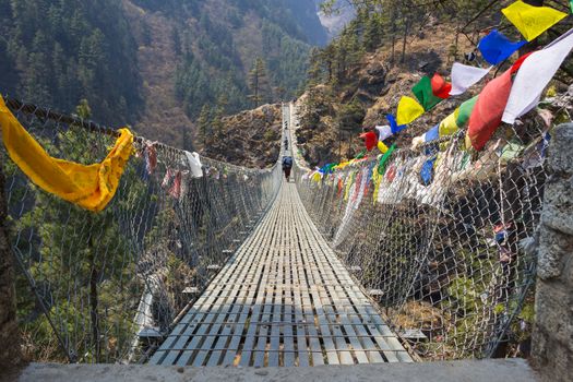 Suspension bridge over the precipice with colorful flags in nepal in  green forest and hills.