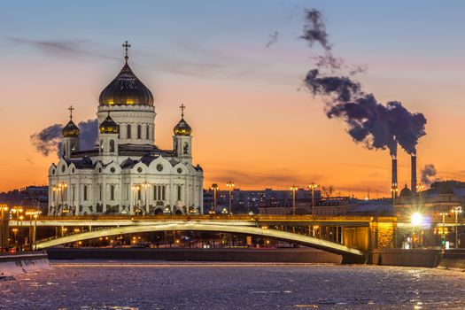 Cathedral of Christ The Savior and Moscow river at frosty winter sunset. Smoke of power plants.