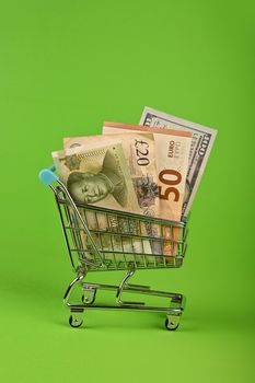 World paper currencies in shopping cart over green