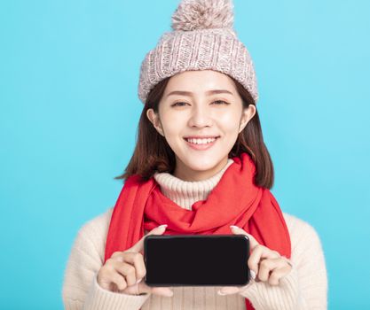 Smiling young woman in winter dress and showing  smart phone