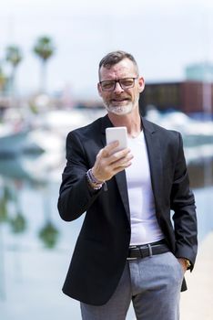 Mature businessman using cell phone while standing outdoors against harbor