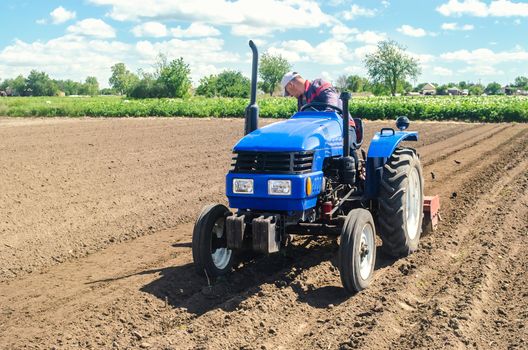 Farmer on a tractor loosens the soil with milling equipment. Loosening surface, land cultivation. Farming, agriculture. Plowing field. Use of agricultural machinery and to simplify and speed up work.