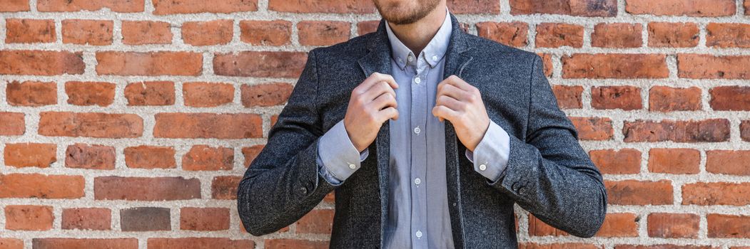 Suit man young businessman adjusting his blue coat smart casual outfit against brick wall background banner panorama at office. Urban lifestyle