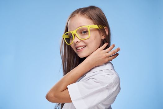 Cheerful little girl in white shirt glasses Studio blue background fun childhood
