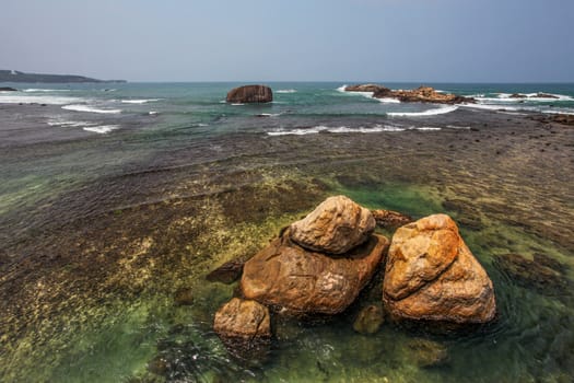 Huge rocks in clear sea near shore, with horizon in distance. Ga