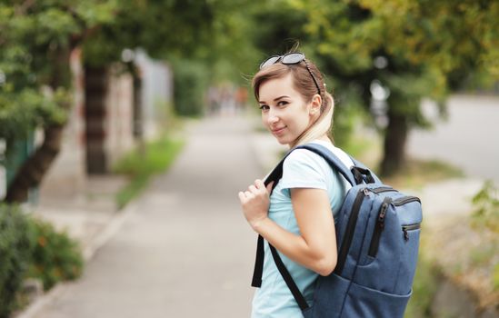 Portrait of a young stylish woman walking down the street with a backpack.