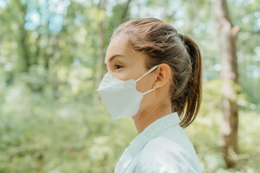 Asian woman wearing face mask walking in outdoor nature. Eco-friendly sustainable masks concept. Woman with korean kn95 mouth covering for corona virus prevention in forest