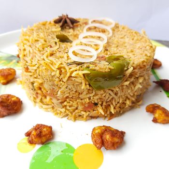 Colorful Delicious yummy prawn briyani with prawn fry in center with prawn fry and raita plated beautifully in white plate with bayleaf and it's one of favorite restaurant cuisine food