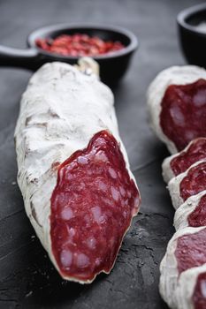 Dry cured salchichon sausage slices with herbs on balck background
