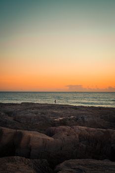 Single person over a massive rocks in front of the sea with a sunset over the horizon