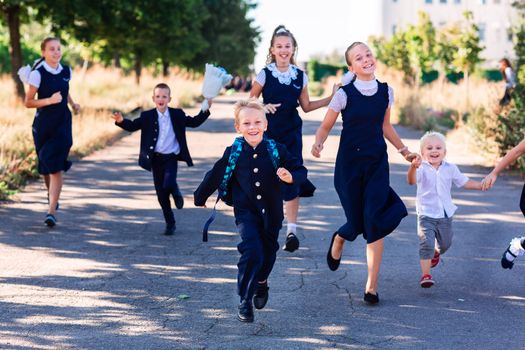 Happy little schoolchildren running together to school
