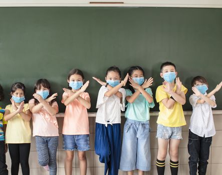 Group of diverse young students wear mask and showing stop sign gesture in classroom