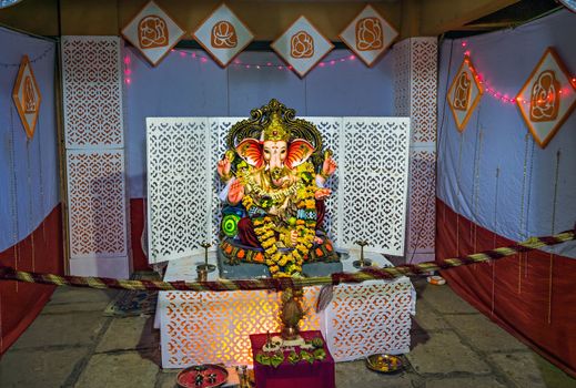 Garlanded deity idol of Lord Ganesha installed with background decorations for festival.