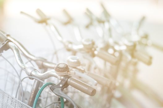 Vintage bicycles standing in row one after another. First bike with classic straight handle bar, hand-brake and bell in foreground, other vehicles blurred. Retro style objects. Sport and activity.