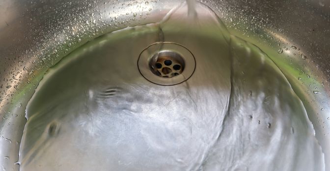 Running water from a water tap into the drain of a chrome sink.