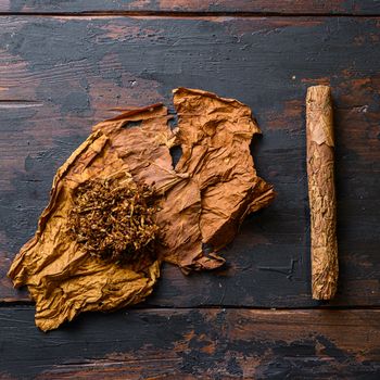Cut tobacco and tobacco leaves with cigar on wood background on vintage dark table. overhead shot top view