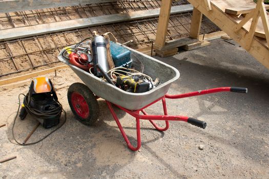 A close-up view shows a wheelbarrow loaded with construction tools. The concept of repair.