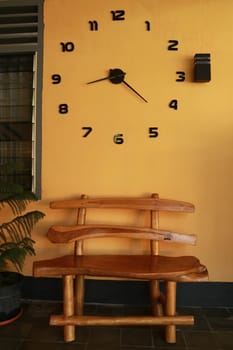 wooden bench near yellow wall. Vintage wooden bench under the wall clock